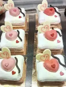 Pâtisseries spéciales Saint-Valentin, délicats entremets en forme de cœur, décorés de chocolat blanc et rouge avec des inscriptions romantiques, parfaits pour une pause sucrée en amoureux.