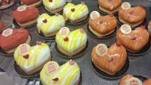 Plateau de petits entremets en forme de cœur, glacés blanc à filets jaunes et orange, chacun décoré d’un petit cœur et d’une pastille “Bonne Fête maman”