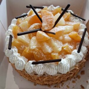 Vue plongeante d’une tarte garnie de moitiés d’abricots caramélisés, de touches de crème chantilly, de bâtonnets de chocolat et d’amandes effilées