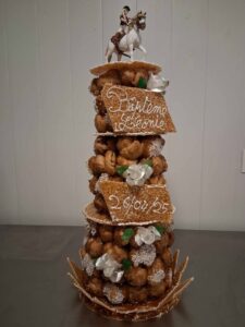 Pièce montée de choux caramélisés assemblés en cône, agrémentée de nougatine gravée “Baptême Léonie 26/04/25” et surmontée d’une figurine de cavalier