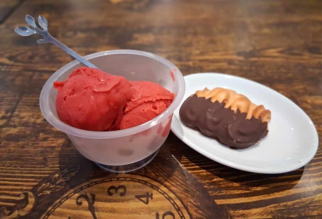 Coupe transparente de sorbet framboise accompagnée d’une meringue partiellement enrobée de chocolat sur une petite assiette blanche