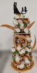 Pièce montée de mariage avec un couple de mariés et leurs enfants en silhouette, décorée de choux, de fleurs blanches, de perles bleues et de motifs en nougatine en forme de cœur et de croissants.