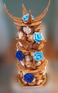Pièce montée sur le thème de la mer, décorée de choux, de morceaux de nougatine et de roses en sucre bleues, évoquant des vagues ou des éléments marins.