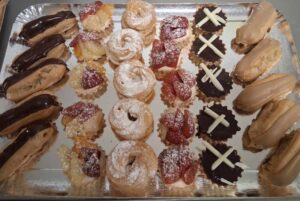 Plateau argenté assorti de mini pâtisseries, incluant des éclairs au chocolat, des éclairs au café, des religieuses ou choux, des tartelettes aux fruits (fraises, ananas), et des tartelettes au chocolat blanc et noir.