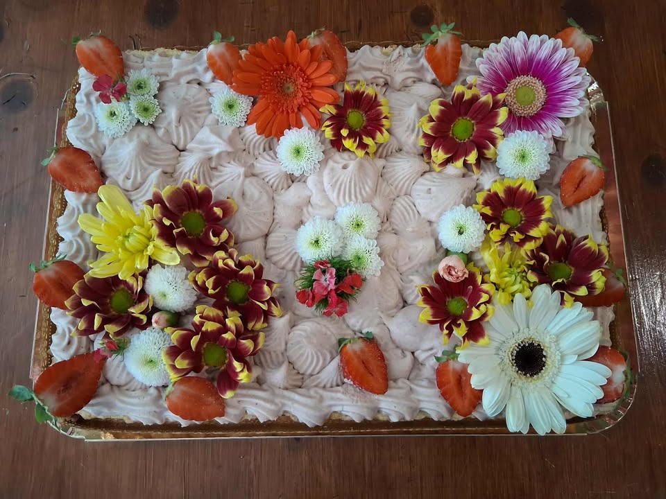 Gâteau à la crème rose décoré de fleurs fraîches colorées et de fraises sur un plateau.